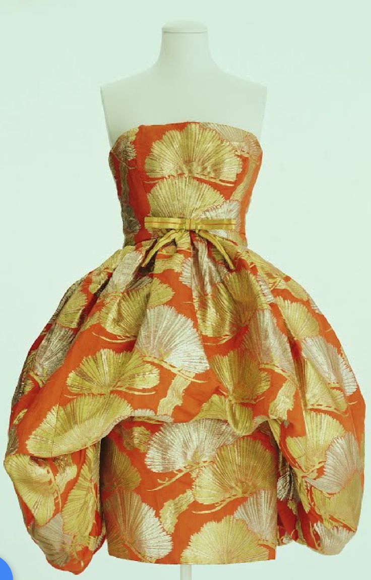 a vintage strapless dress in orange with gold leaf pattern on a mannequin. the dress is in a prom style with a full skirt.