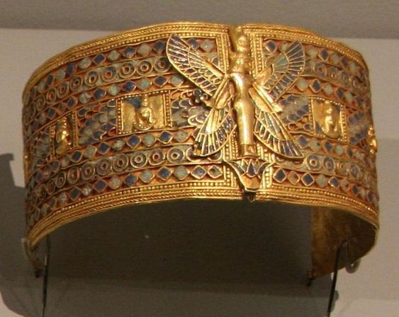 the image shows a golden diadem from the hellenistic period.  it has repeating circular patterns and a central goddess figure with spread wings.