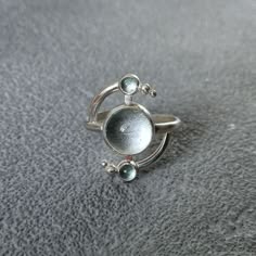 a closeup of a silver ring with an aquamarine gemstone and smaller aquamarine stones set in a crescent moon design. the ring is on a gray background.