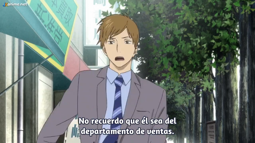an anime still featuring a young man in a suit and tie. he is walking down a city street lined with trees, with buildings in the background. the man has a surprised expression on his face. the lighting suggests it's daytime with the sun shining. the overall palette consists of muted greens, blues, and browns.
