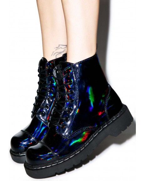 the image shows a pair of shiny black holographic platform combat boots laced up, with a tattoo visible on the wearer's ankle. the boots have a chunky black sole and white stitching.