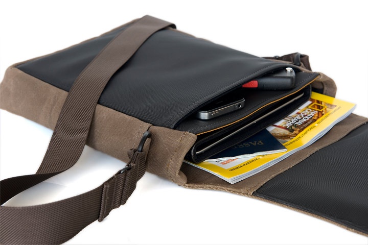 this is an image of an open brown leather bag.  the bag is made of brown leather and has a brown strap. the bag is open, and the inside is visible. the inside of the bag contains a phone, passport, and travel guide. the bag is designed for travel and has many compartments for storing different items.