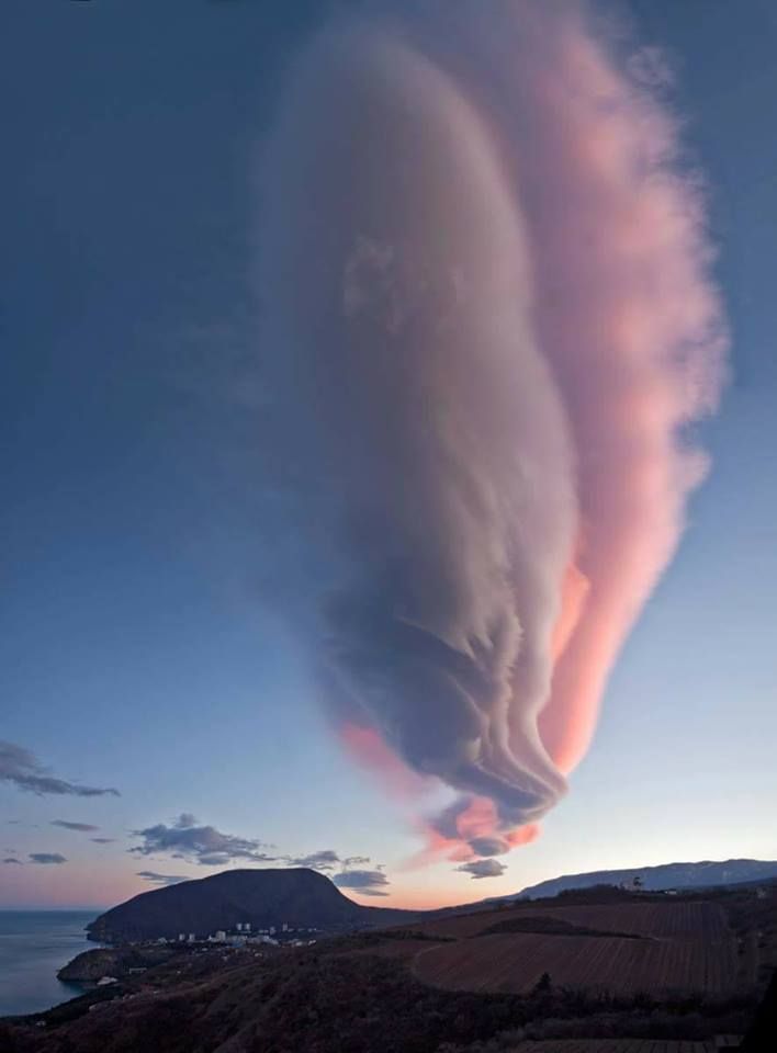 a breathtaking view of a dramatic sky with lenticular clouds, which are also called  lensshaped clouds. they are created when stable air flows over a mountain or hill. the clouds are a vibrant pink and white color, with a touch of blue as they sit above the horizon.  the clouds create a sense of mystery and beauty, a beautiful sight to behold.