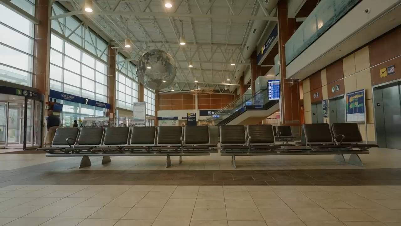 the image showcases the spacious interior of a modern airport terminal. rows of empty seats occupy the foreground, inviting travelers to rest. a large, suspended globe serves as a captivating focal point, drawing the eye upwards towards the high ceiling and expansive windows. the abundance of natural light creates a bright and airy atmosphere, enhancing the sense of openness.  to the right, an elevator and stairs lead to the upper levels, hinting at the bustling activity beyond the frame.  the overall impression is one of modern efficiency and anticipation, characteristic of travel hubs.