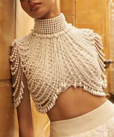 a woman is wearing a beautiful pearl necklace and top. the pearls are strung together in a delicate pattern that cascades down her chest and shoulders. she is also wearing a white skirt that is long and flowing. her skin is fair and her lips are a soft pink. she looks sophisticated and glamorous.