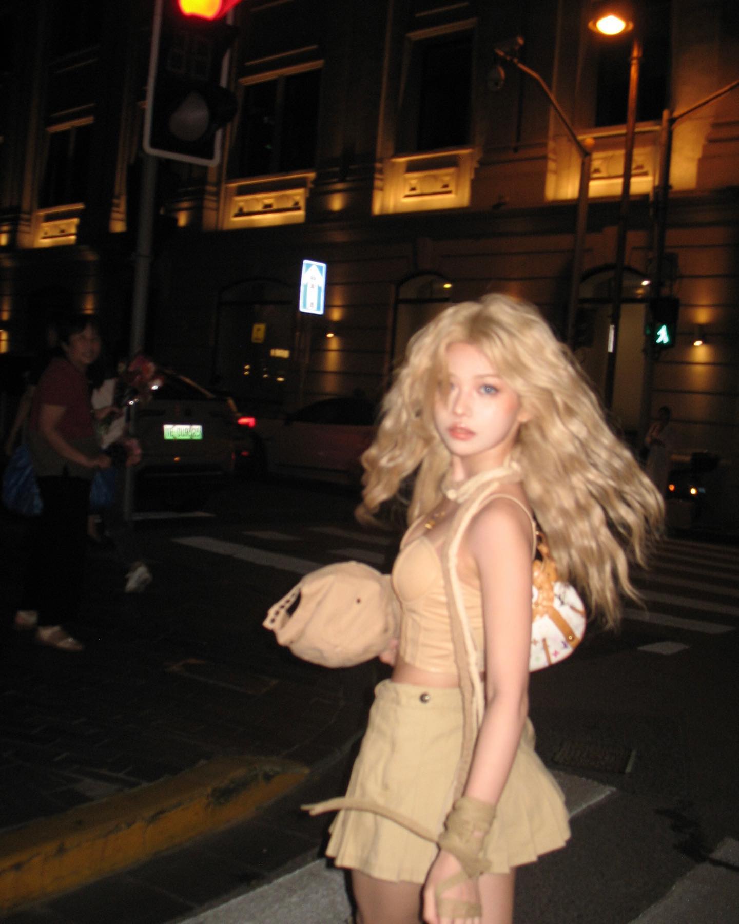 a young, blonde asian woman is captured standing on a city street at night.  she is dressed in a stylish y2kinspired outfit. the warm glow of streetlights illuminates the scene and highlights the details of her clothing and the urban surroundings.  the image exudes a sense of urban cool and captures a moment of contemporary street fashion.