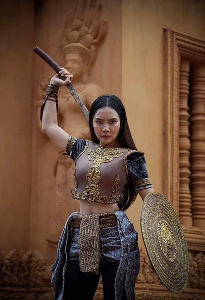 an asian woman dressed as a warrior, holding a sword and shield, stands in front of a temple. she wears traditional armor and has a serious expression on her face, ready to fight. the scene is visually striking, emphasizing the woman's power and confidence.