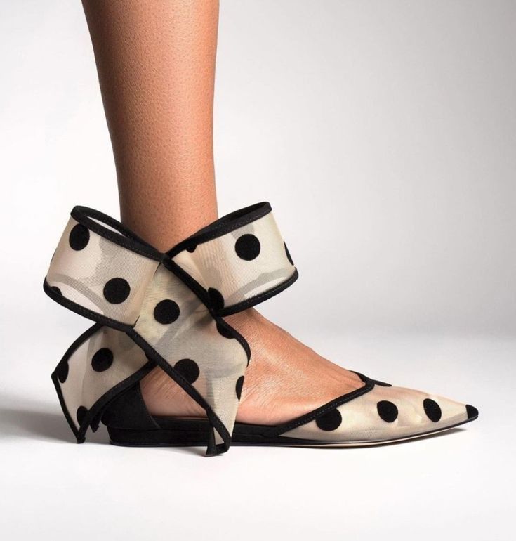 a close up image of a woman's foot wearing black polka dot mesh ballerina flats with a bow ankle strap. the background is white.