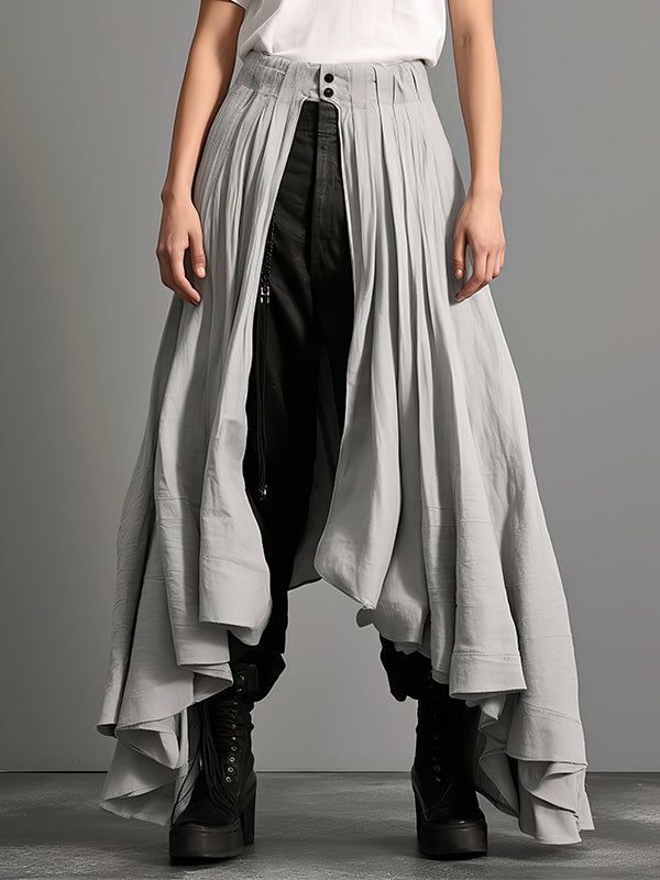 a person stands in a gray, pleated, asymmetrical skirt that is open in the front to reveal dark pants and black boots. the skirt is highwaisted with two buttons visible at the top. the outfit suggests avantgarde fashion.