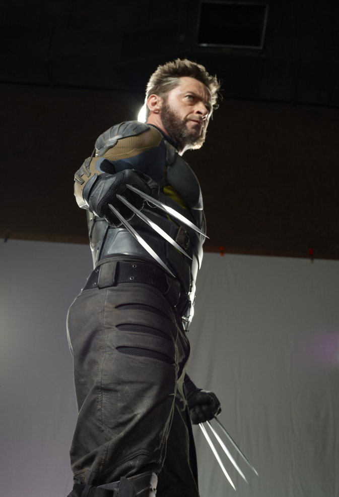 a fullbody studio shot of hugh jackman as wolverine in costume, with his claws extended, looking away in an action pose.