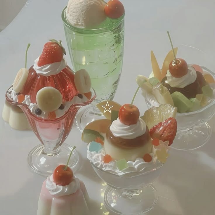 the image shows an arrangement of different desserts. there's a tall glass filled with a green liquid, topped with a scoop of ice cream and a cherry. there are also several fruit parfaits in glass dishes, decorated with pudding, whipped cream, various fruits like strawberries, bananas, kiwi, and cherries, and small candies. one dessert appears to be a simple pudding with whipped cream and a cherry on top.