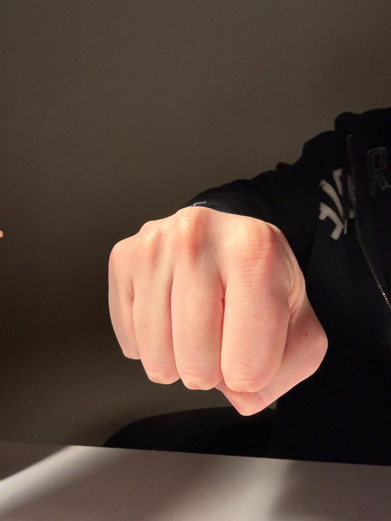 a close up of a clenched fist resting on a table. the fist is illuminated by a strong shaft of natural light that casts a dramatic shadow onto the surface below. the image conveys a sense of strength, power, and determination.