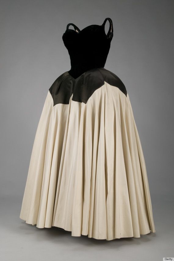 a sleeveless couture dress with a black velvet bodice and a full, ivory pleated skirt stands against a neutral gray background. the bodice has an unusual neckline with straps, and the skirt is voluminous with deep pleats, giving it a bell shape. the dress appears to be a vintage design. a "getty" watermark is present in the lower right corner.