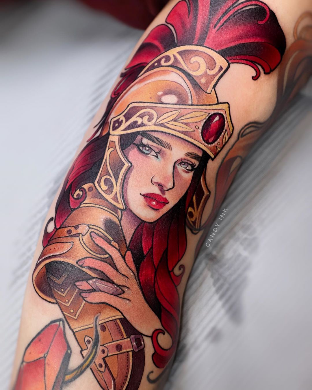 a tattoo of a female spartan warrior on someone's arm. the warrior has red hair and is wearing gold armor and helmet.