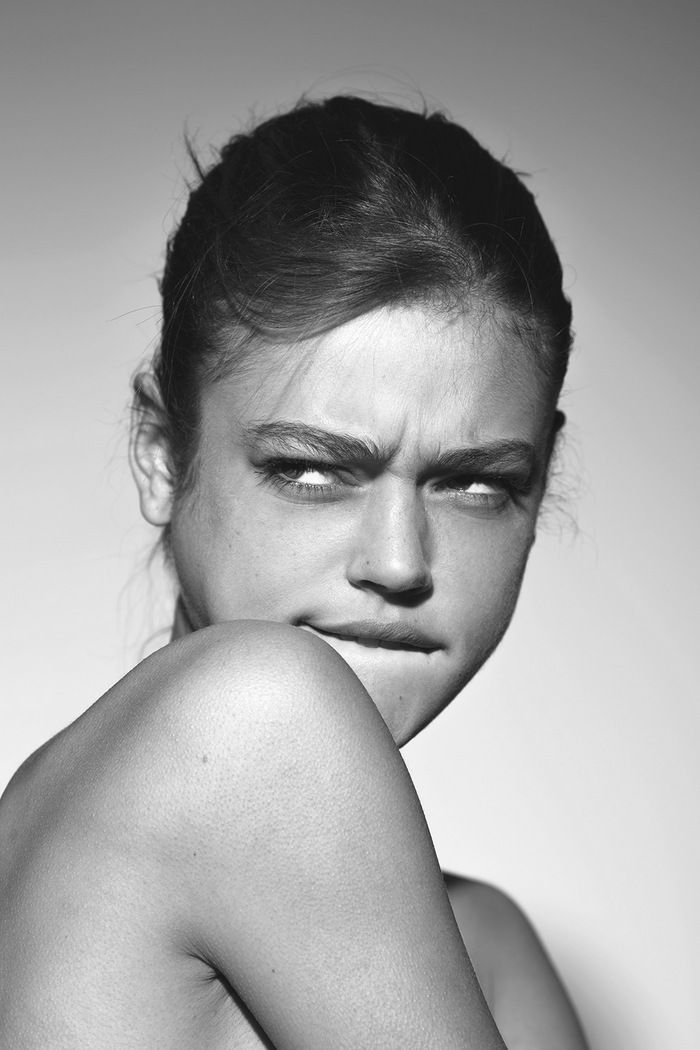 this is a black and white portrait of a young woman. she is looking away from the camera and has a thoughtful expression on her face. her hair is pulled back away from her face, and she is wearing no makeup. she is looking off to the side. her skin looks very smooth and clear.  this is a classic portrait, focused on her face and her gaze. the lighting is soft and even, which highlights her features and gives the image a timeless feel.