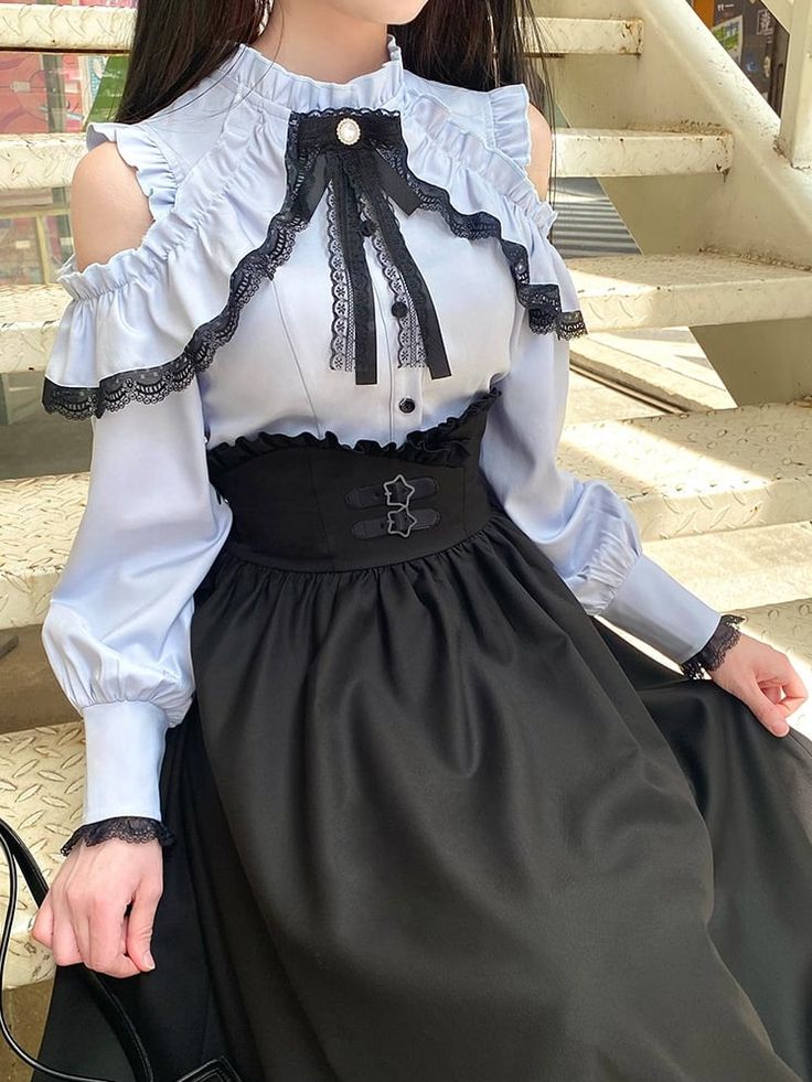a young woman poses on an outdoor staircase while modeling a lolita fashion outfit. the outfit features a light blue blouse with lace trim, a black corsetstyle belt, and a black maxi skirt.