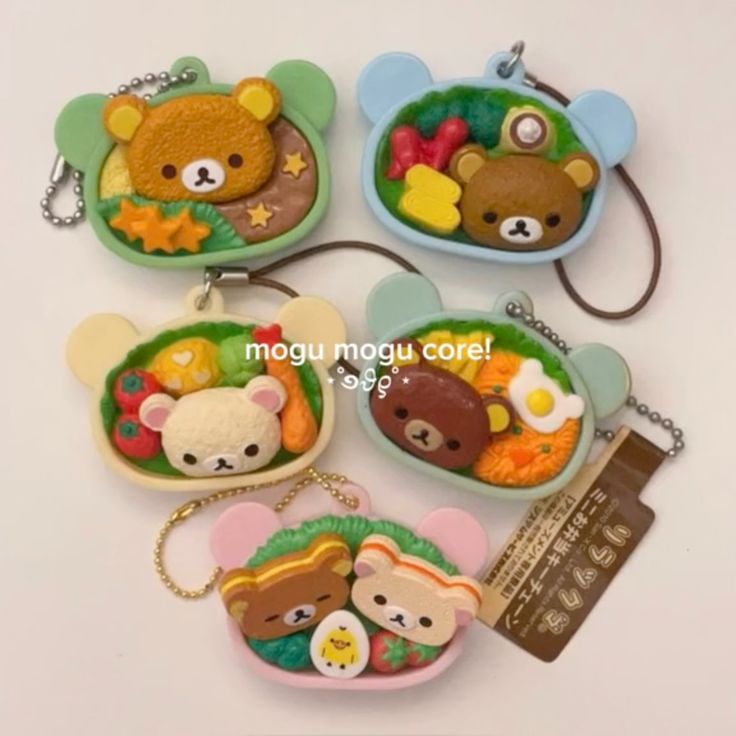the image shows five rilakkumathemed bento box keychains. each keychain features a bearshaped container with various food items and a small rilakkuma character inside. the keychains have different colors and unique food arrangements, adding to their charm.