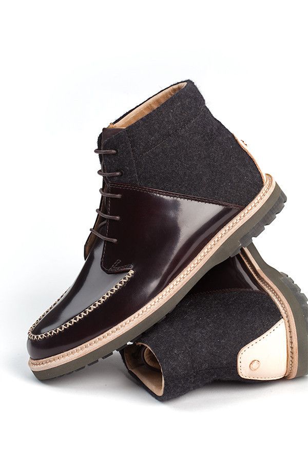 the image showcases a pair of men's hightop boots. the boots are a striking combination of dark burgundy polished leather and dark grey wool.  the leather portion features a moc toe design with visible stitching along the toe seam.  the wool is visible on the upper portion of the boot shaft. the boots have a lightcolored, possibly cream or beige, rubber sole with a visible stitching detail along the edge where it meets the upper. the boots are positioned on a white background with one boot slightly stacked on top of the other. the overall style is a blend of casual and sophisticated.