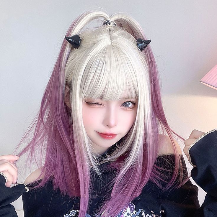 the image showcases a young woman with a striking hairstyle. she sports a blonde wig styled with straight bangs framing her face. the sides of the wig feature a gradient transitioning into a vibrant purple hue. her playful look is accentuated by small black devil horn hair clips positioned atop her head. she has a light complexion and is wearing makeup, including light eyeshadow and lip tint. the woman is dressed in a black longsleeved top and is posing for a selfie indoors, against a backdrop that suggests a room with soft, artificial lighting.