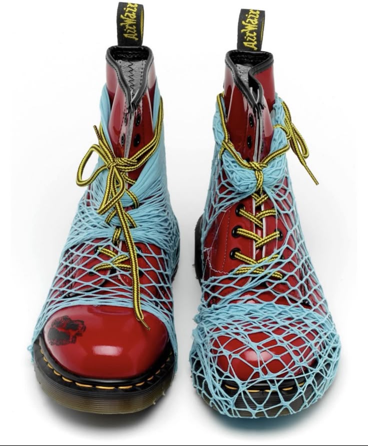 two red patent leather dr. martens boots are displayed. they are laced with yellow laces and wrapped in light blue yarn in a netted pattern.