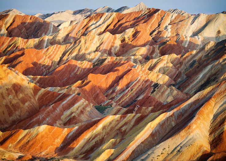 the image shows a landscape view of the colorful zhangye danxia landform geological park. the mountain range features multicolored sandstone formations in shades of red, orange, yellow, and white. the layers and patterns of the geological formations create a visually striking and scenic landscape.