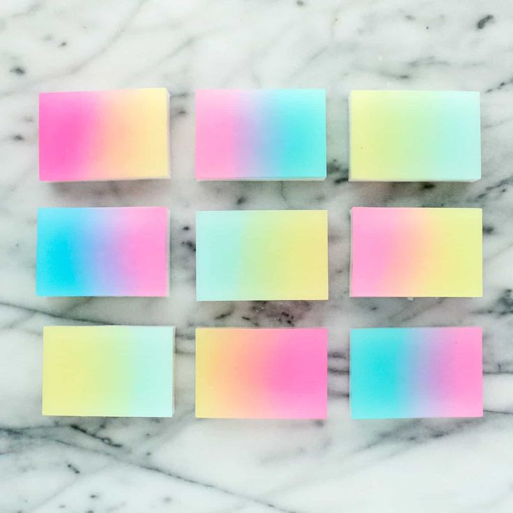 the image is an arrangement of nine ombre soap bars. each bar has a different gradient color scheme, ranging from pastel pinks, yellows, and blues. they are arranged in a 3x3 grid on a white marble background. the image is aesthetic and colorful.