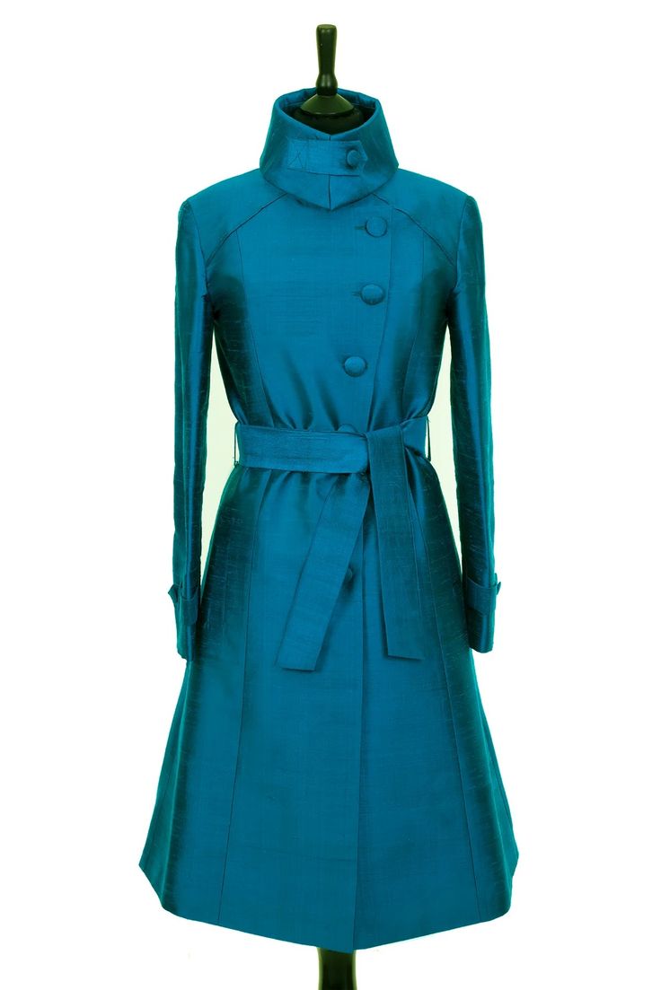 a teal blue women's coat with a standup collar, a belt, and buttons is displayed on a mannequin against a white background. the coat is long and elegant, and it would be perfect for a special occasion.