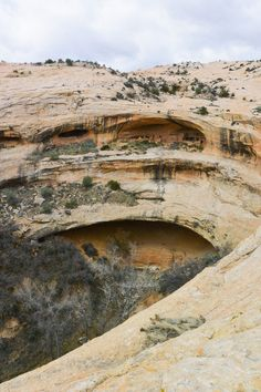 the image shows a landscape with large rock formations, featuring a prominent cave or natural arch in the middle ground. the rocks appear to be composed of sandstone and the surrounding area suggests a desert environment. there are signs of erosion throughout the terrain. the overall scene is a rugged and natural landscape.