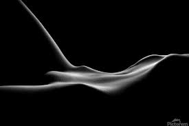 the image is a black and white photograph of a female nude body.  the body is positioned such that it forms flowing, undulating lines against a stark black background.  the lighting is carefully used to highlight the curves and contours of the body, creating a sense of both abstract form and sensual suggestion.  the overall effect is minimalist and elegant, with the focus on the beauty of the human form. the image uses strong contrast between light and dark to create a dramatic and evocative mood.  details are minimized, allowing the viewer to focus on the overall shapes and curves.