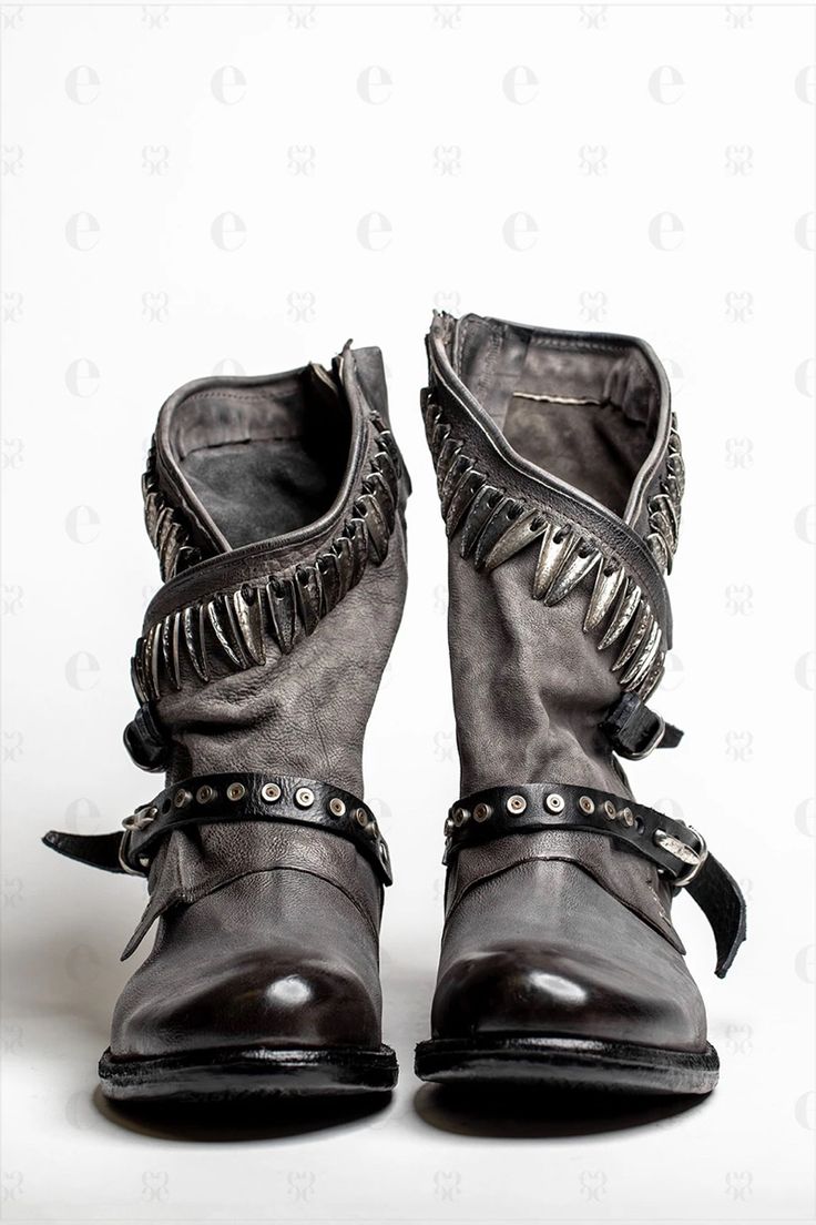 a pair of gray leather ankle boots with silver studs and buckles are displayed against a white background. the boots are distressed for a vintage look.  they have a zipper closure and a chunky heel. the boots are positioned upright, showcasing their details.