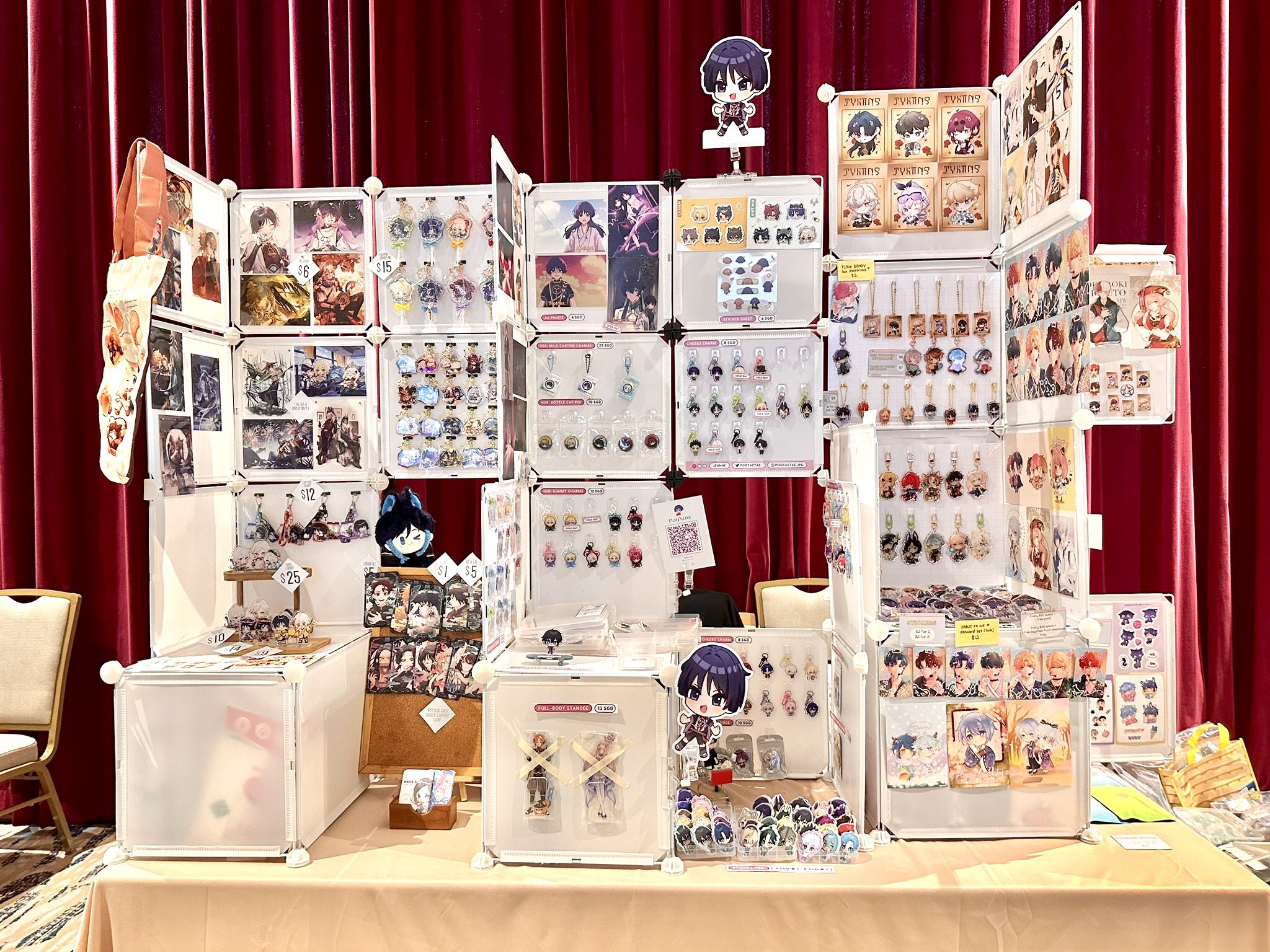 a booth at an anime or manga convention. the booth is set up with a variety of anime merchandise, including pins, keychains, figures, and posters. the booth is decorated with anime characters and artwork. the booth is set up in a way that is eyecatching and inviting to potential customers. the booth is manned by a vendor who is knowledgeable about the merchandise and is able to answer any questions that customers may have. the vendor is excited to share their passion for anime with others.