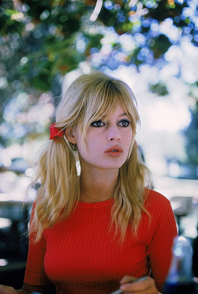 a beautiful blonde woman in a red shirt looks at the camera with a smile. she is outdoors on a sunny day. she has a beautiful smile and she is happy.