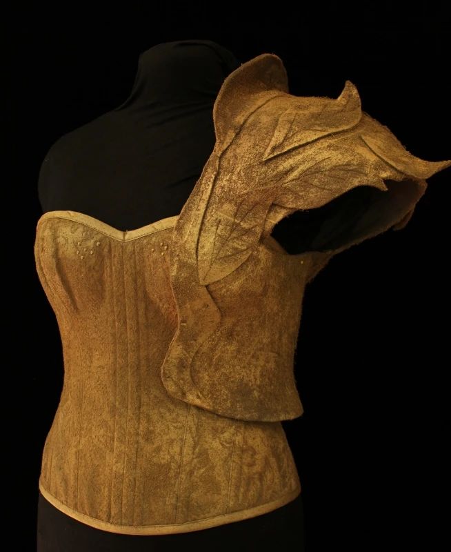a tan corset and armor are displayed on a mannequin. the armor is shaped like a leaf and covers the right shoulder. the background is black.