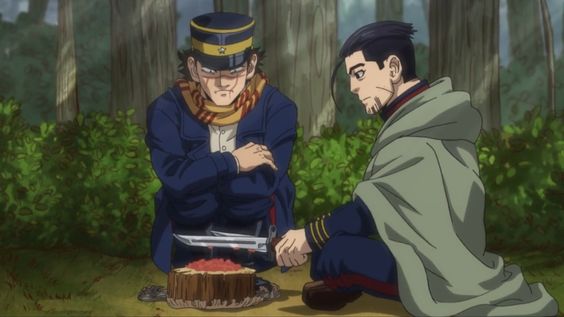 two men in military uniform are sitting in the forest. one is cutting some kind of meat on a tree stump, while the other one watches him.  there is greenery around them and the scene is lit by natural light.