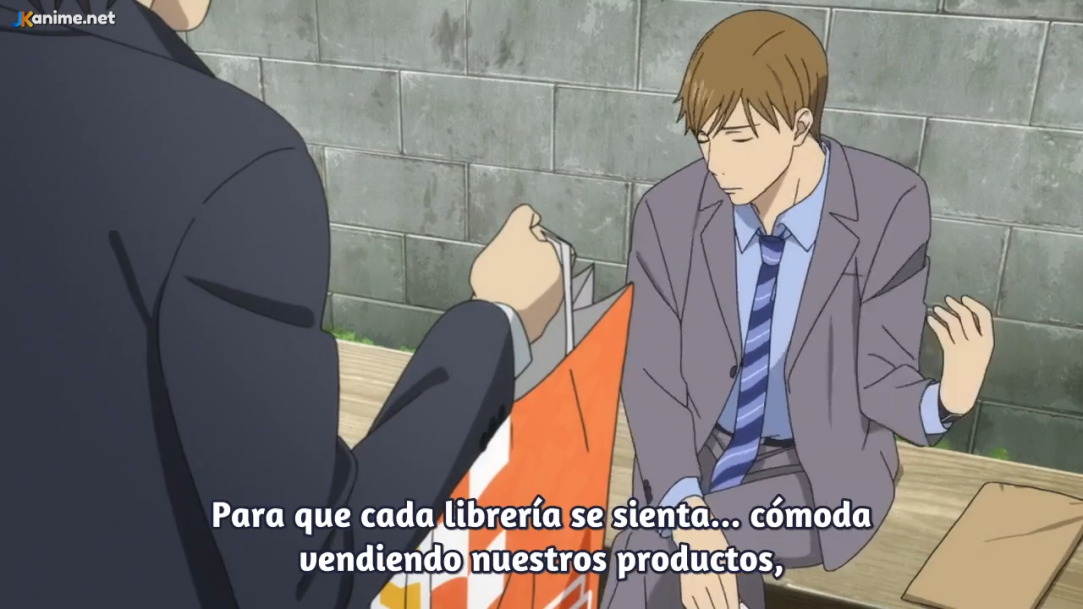 two men in suits having a conversation outside. one man is sitting on a bench and holding a bag while the other is standing with his back to the camera. the background is a grey brick wall.  the image appears to be a still from an anime. there are spanish subtitles at the bottom of the image.