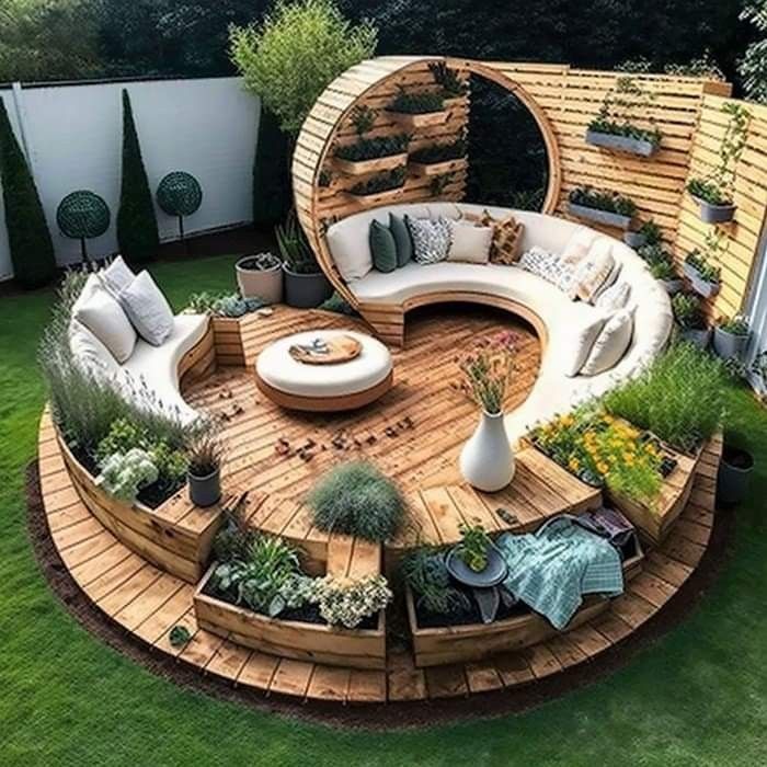 the image showcases a beautifully designed outdoor living space featuring a circular wooden deck with curved couches and raised garden beds. the deck is surrounded by green grass and a white fence with conical shrubs. a wooden pergola partially covers one of the couches, which is adorned with comfortable cushions and throw pillows. raised garden beds with various plants add a touch of nature to the space. additional features include a round ottoman, wooden planters, and a wooden screen with container gardening. the overall design creates a modern and inviting outdoor retreat.