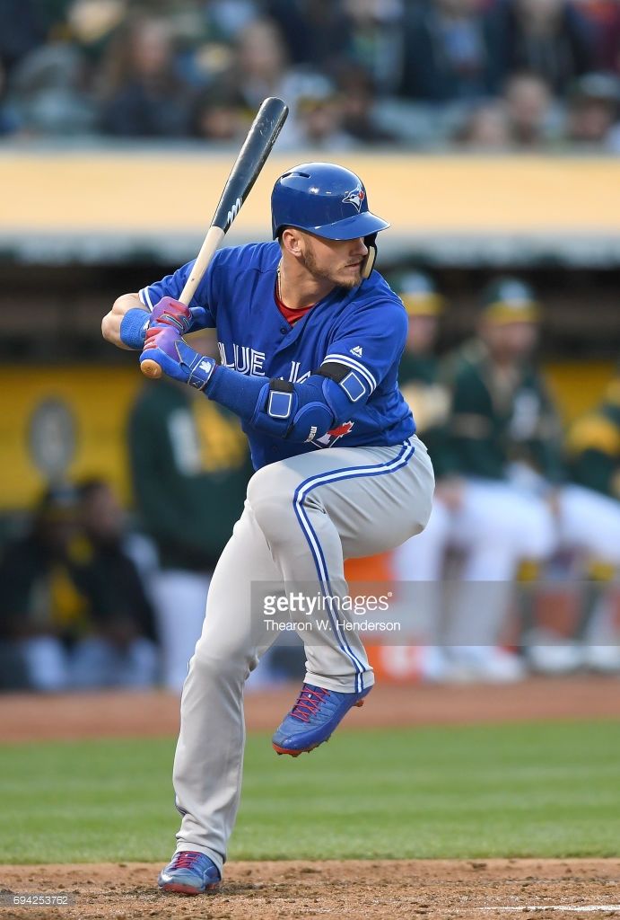 a baseball player in a blue and white uniform is caught in the middle of his swing. he is holding a wooden bat and is wearing a helmet, batting gloves, and eye black. the background is a blurred baseball field with green grass and brown dirt.