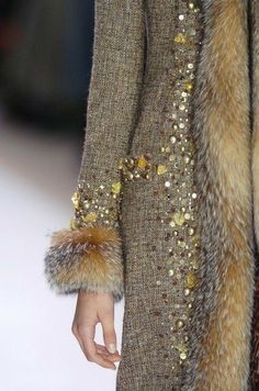 a closeup shot of a woman's brown coat with a fur trim. the coat is adorned with gold sequins, creating a luxurious and elegant look. the fur trim is soft and fluffy, adding a touch of warmth to the outfit. the image captures the intricate details of the coat's design, showcasing its high quality and craftsmanship.