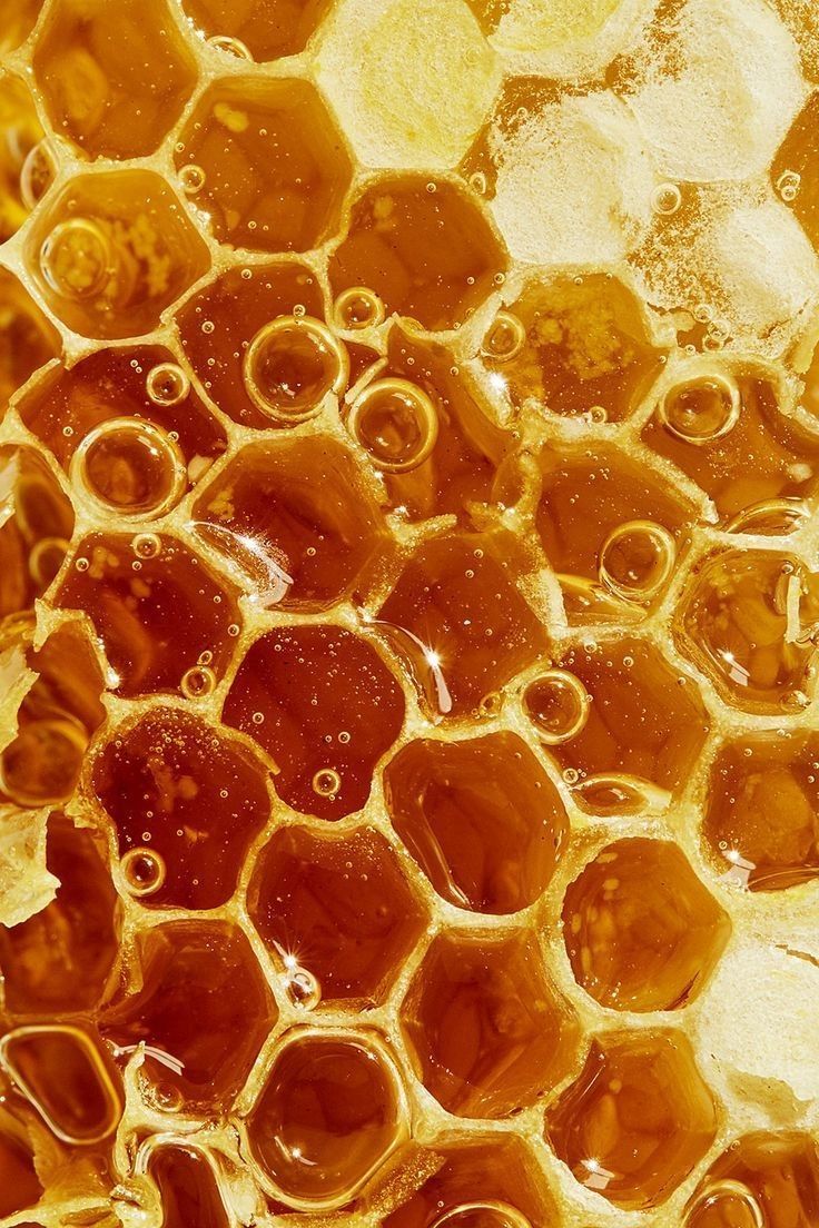 a closeup shot of a honeycomb filled with golden honey. the hexagonal cells are clearly visible, with numerous bubbles trapped within the honey. the texture is rich and detailed, highlighting the natural pattern and sweetness of the honey.