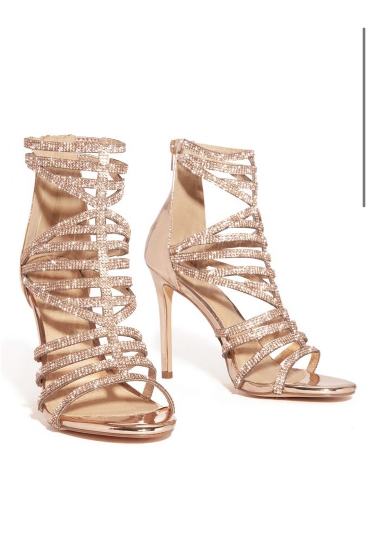 a pair of rose gold rhinestone embellished strappy high heels. the shoes are a delicate shade of rose gold with sparkling rhinestones covering the straps. they are high heels with a stiletto heel and ankle strap.  the shoes are shown from a slightly angled perspective, showcasing both shoes and the intricate detailing of the rhinestone work. the background is a plain white, drawing focus to the shoes.