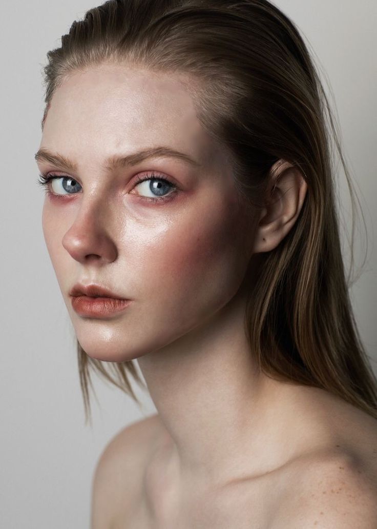 a closeup portrait of a young woman with light brown hair styled wet and pulled back from her face.  she has minimal, naturallooking makeup with rosy cheeks and dewy skin. the background is a simple, neutral gray. the overall impression is one of clean, natural beauty.