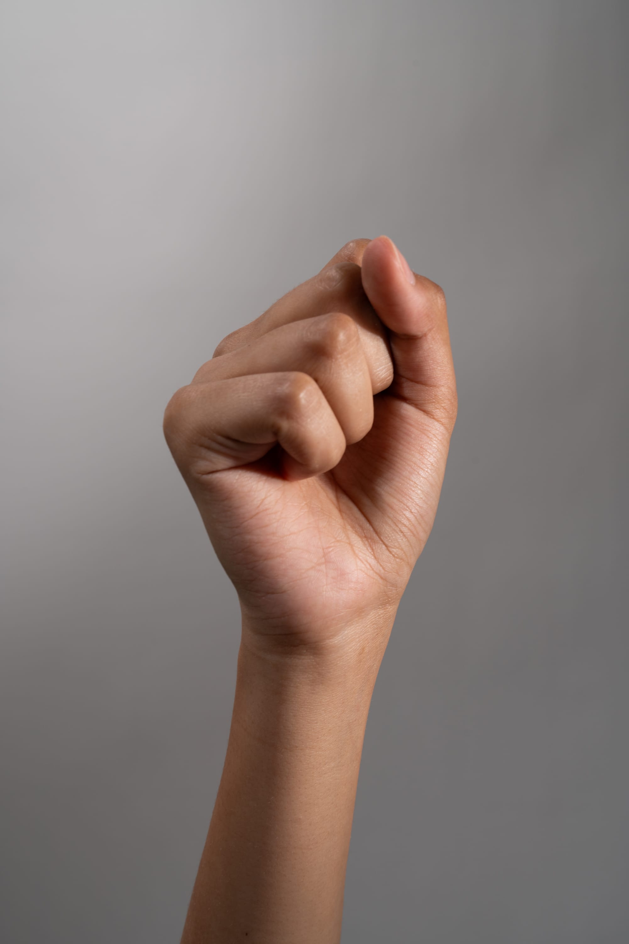 a hand is making a fist against a gray background. the image is lit with studio lighting and taken at closeup.