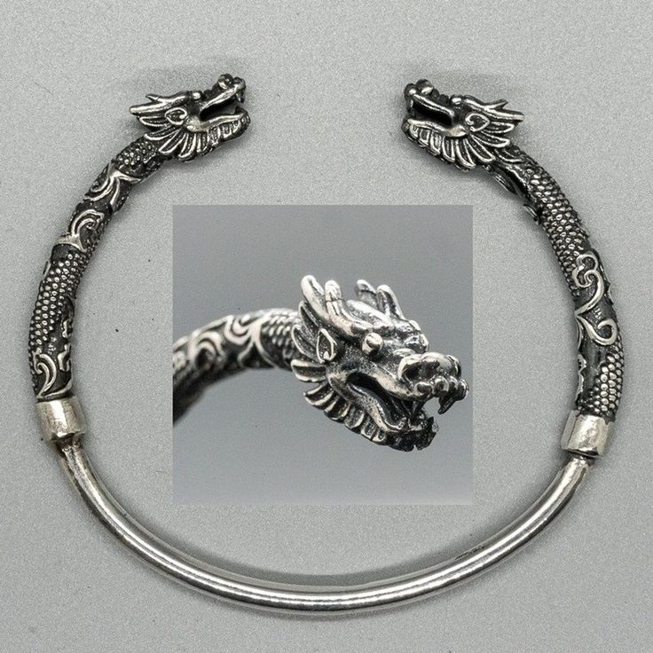 a silver cuff bracelet with dragon head ends. the dragon heads are ornate and detailed. the body of the bracelet near the dragon heads is decorated with scales and other designs. the bracelet has a silver band in the middle.