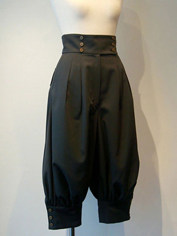 closeup shot of a pair of black highwaisted pants on a mannequin. the pants are pleated, have a sailorstyle button detail at the waistband, and balloonstyle legs with cuffs. the overall style is vintage or retro. the pants are made of a smooth, possibly satinlike fabric. the mannequin is a simple white form, allowing the clothing to be the main focus. the background is a plain, lightcolored wall.