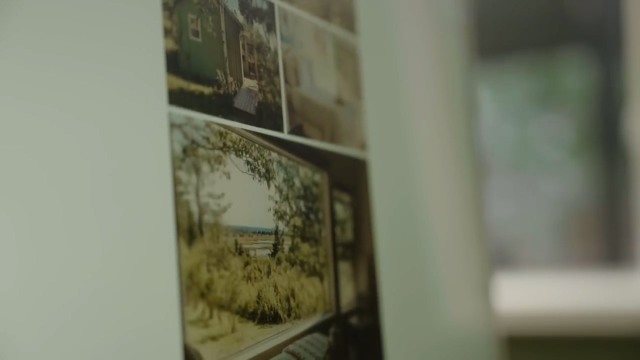 a collage of photos are tacked to a wall. the photos show a building surrounded by nature. the photos have a vintage look with a yellowish tint.  the photos are slightly blurry. to the right of the collage is a doorway. the room is welllit.