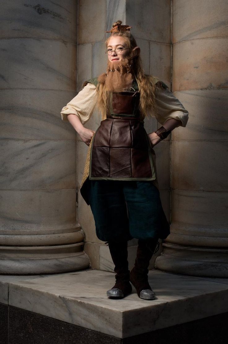 a fullbody portrait of a young woman cosplaying as a fantasy character, possibly an elf or dwarf. she is wearing a unique costume that blends medieval and steampunk elements.  the costume includes a leather apron over a longsleeved shirt, tealcolored trousers, and dark boots with metallic accents. she is wearing a fake beard and glasses, and her hair is styled up.  the backdrop is a marble columned hallway. the lighting casts shadows on the stone, creating a dramatic effect.  her posture and expression are serious and confident.