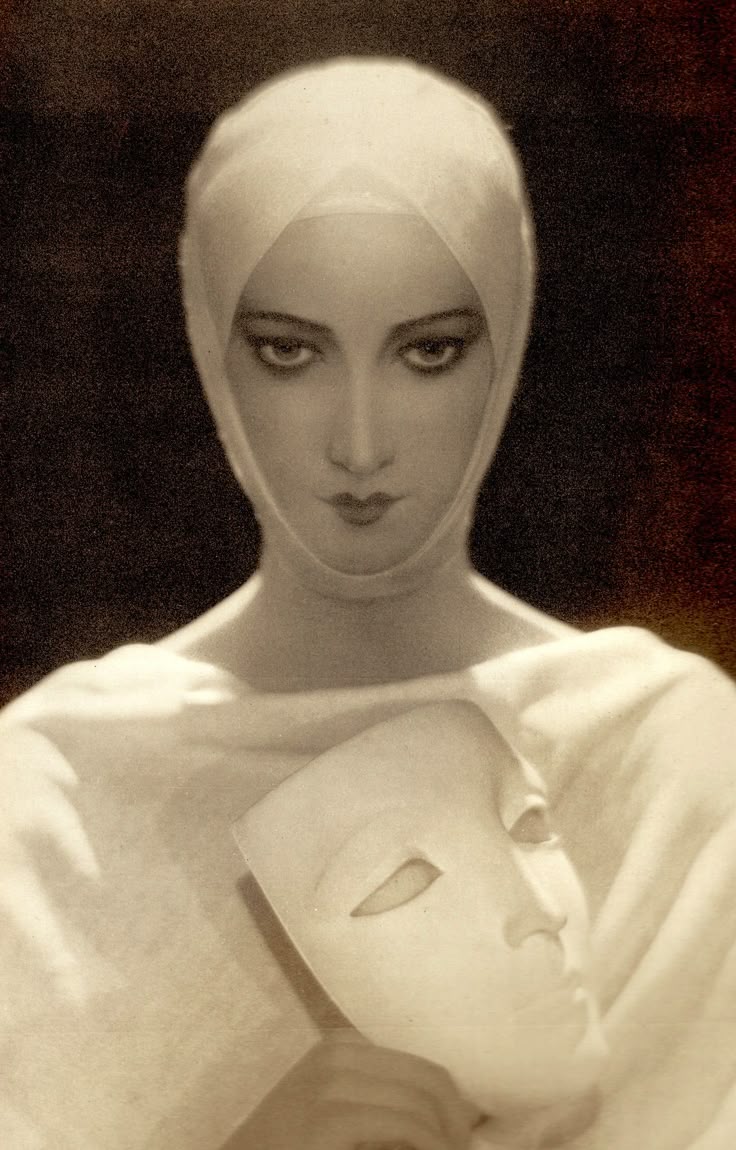 a vintage sepia portrait depicts a woman with a serious expression, her head wrapped in a white covering. she holds a white mask close to her body, obscuring part of her torso. the background is dark and indistinct, adding to the mysterious and slightly surreal atmosphere of the image. the lighting emphasizes her face and the mask, drawing attention to their stark contrast.