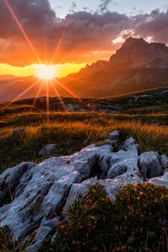 the image showcases a breathtaking mountain landscape bathed in the warm glow of sunset. the setting sun casts a golden hue across the sky, illuminating the rugged peaks and grassy slopes. the foreground features a rocky outcrop, adding texture and depth to the composition. the overall scene evokes a sense of tranquility and aweinspiring beauty.