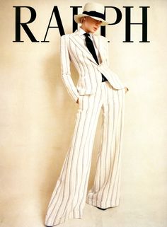 a woman wearing a white striped suit with a white hat stands in a studio with a beige background.