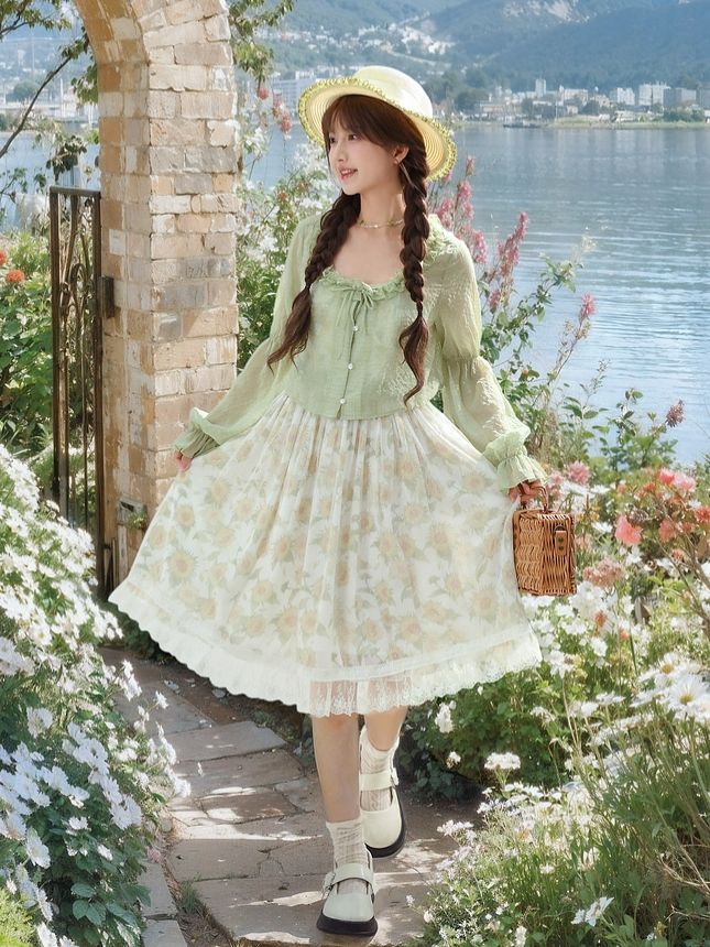a young woman is posing in a gardenlike setting, framed by a stone archway. she is wearing a flowing green and white floral dress and a straw hat. the background features a serene view of mountains and water. the overall aesthetic is light, airy, and summery.